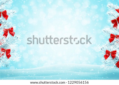 Christmas tree branches with red bow decorations. Blue background with snowflakes, light and bokeh.