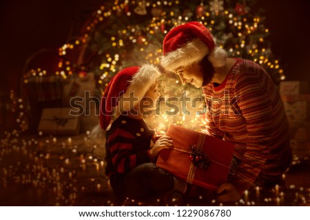 Family open Christmas Lighting Present Gift Box front of Xmas Tree, Happy Mother with Baby Child in Magic Night