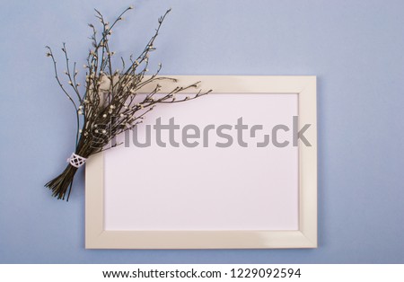 A small bouquet of dried flowers lies on top of a white frame, which is on a blue background.