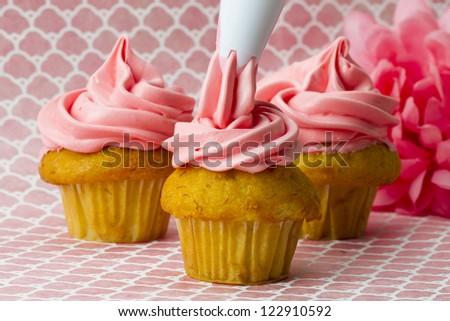 Close-up image of a person decorating cupcakes with an icing tube.