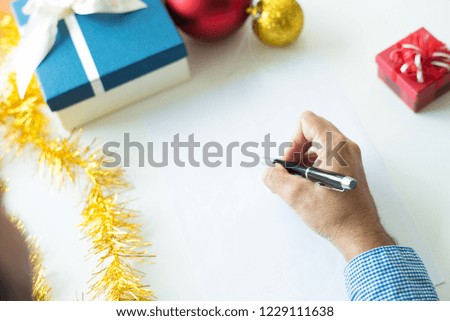 Close-up of businessman writing gift list before Christmas. Unrecognizable man sitting at table with Christmas decorations and making notes. Tasks concept