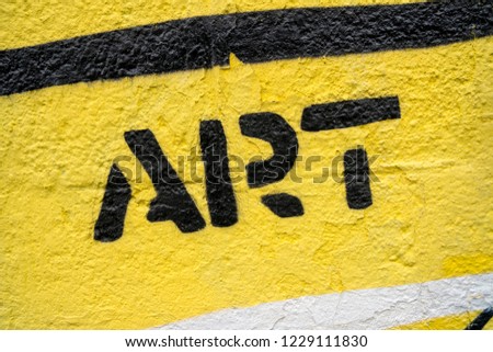 Fragment of graffiti drawing. Word “art” in black on yellow old wall decorated with paint in street art style.