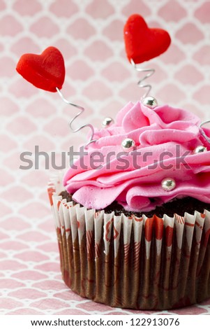 Close-up cropped view of strawberry cupcake with heart shape and shiny metal beads on a pink background.