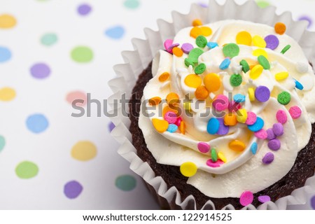Close-up cropped shot of a cupcake with colorful sprinkles over polka dots background.