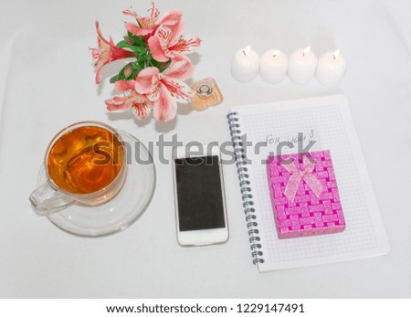 Dressing table with women's accessories. Image of a pink gift box with a bouquet of Alstroemeria flowers, romantic candles, perfume, notepad and cell phone. 