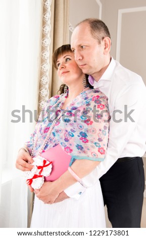 The couple stands in an embrace at the bright window.