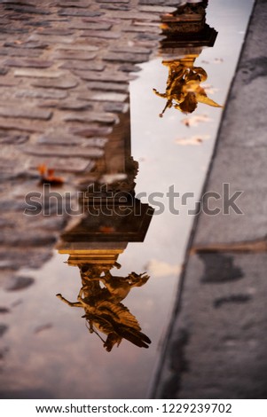 Reflection of winged horse statues of Alexander III Bridge in Paris (France) in water puddle after rain in autumn day at sunset. Romantic abstract Parisian vacation background. Selective focus.