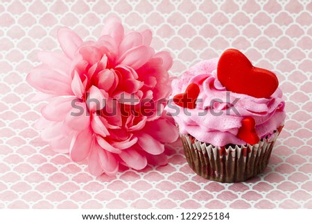 Close-up shot of a strawberry cupcake with heart topping and a flower.