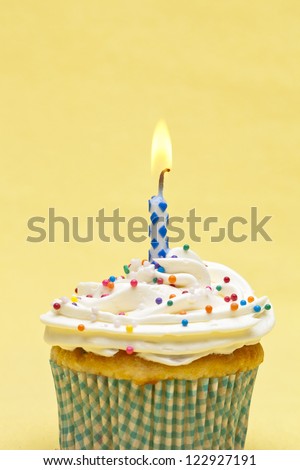 Detailed image of a cupcake with sugar icing and blur burning candle against plain yellow background.