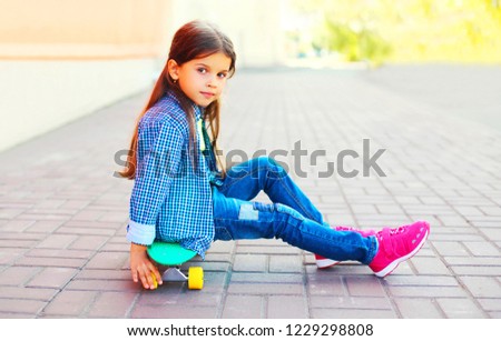 Fashion little girl sitting on skateboard on city street