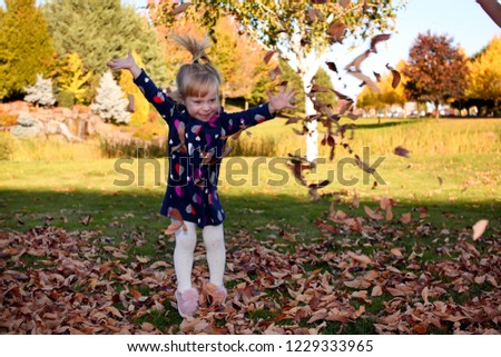 Portrait of Pretty Smiling Cute Toddler Girl playing with leaves in autumn park on the walk, wearing fashion Dark Dress, Portland Oregon