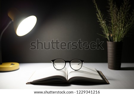 Glasses placed on the book, Open book, A flower vase is placed, And light from the lamp.