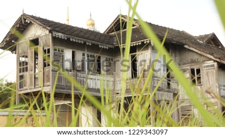 Old abandoned traditional malay house with a mosque in the background