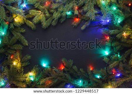 Christmas frame with fir branches and Christmas lights on black background. Copy space for text