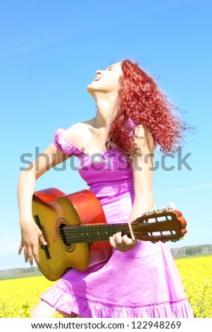 curled redhead woman in a purple summer dress in rapeseed field