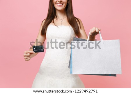 Cropped image of smiling bride woman in wedding dress holding credit card, multi colored packages bags with purchases after shopping isolated on pink background. Organization of wedding. Copy space