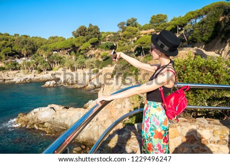 Woman taking pictures of beautiful seashore with rocks and vegetation