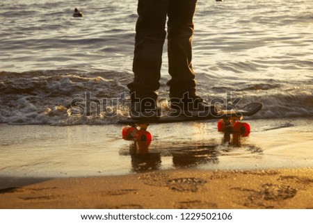 Close-up of the skateboarders ' feet while riding on the beach sand at sunset with the sea wave in the background