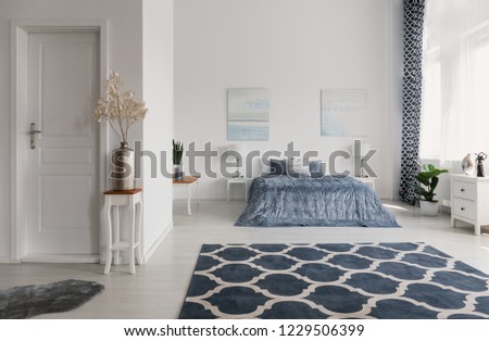Patterned carpet in spacious bedroom interior with plant on table and posters above bed. Real photo