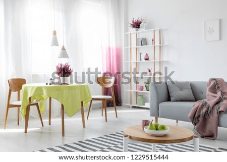 Living and dining room in modern apartment with grey couch and wooden furniture, real photo