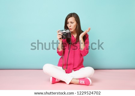 Full length portrait young woman in rose shirt blouse white pants sitting on floor hold camera isolated on pink blue pastel wall background studio. Fashion lifestyle concept. Mock up copy space