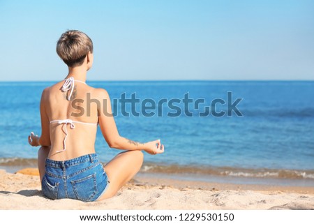Young woman meditating on beach. Space for text