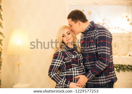 Happy couple in holiday spirit showing affection for one another. Dressed in plaid clothes. Gentle pregnant woman