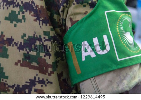 A soldier from the African Union Mission in Somalia (AMISOM), wears a green armband over his camouflage uniform reading AU (African Union), and with the AU flag. Royalty-Free Stock Photo #1229614495