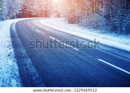 winter road, covered with snow on sunny day. Black icy asphalt