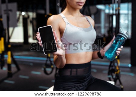 Partial view of sportive woman holding smartphone in fitness gym 