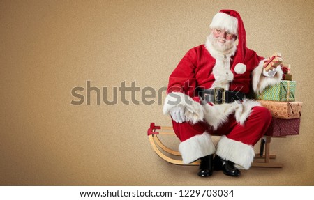 Santa Claus sitting on a sled with Christmas gifts and presents on a plain background with copy space.