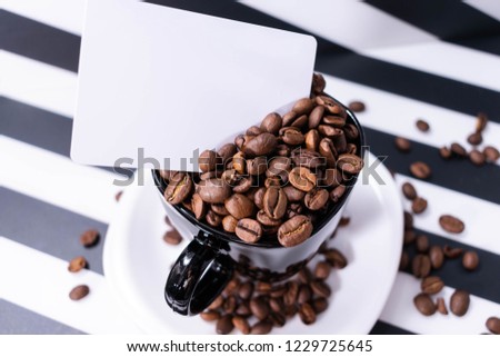 Coffee beans inside and around white cup on striped black and white background