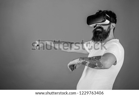 Man with beard in VR glasses driving car, red background. Virtual driving lessons concept. Hipster on confident face driving car in virtual reality with modern digital gadget.
