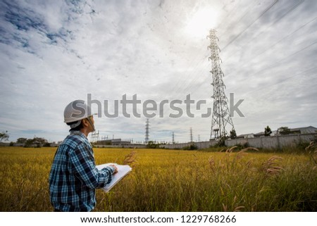 Electrical engineer working. Electrician holding blueprint at high voltage power pylon against blue sky. This can be used as a business card background.