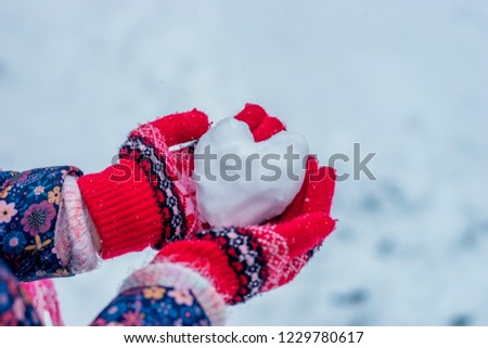 Heart of snow in the hands of the girl. Hands in knitted mittens holding red heart made of snow.