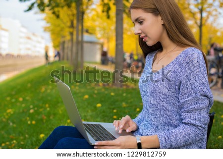 Lovely woman in casual wear professional content manager checks the job of remote workers via laptop computer while sitting in park in autumn day. Pretty female student online learning via notebook 