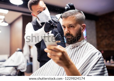 Hipster man client visiting haidresser and hairstylist in barber shop, taking selfie. Royalty-Free Stock Photo #1229824174