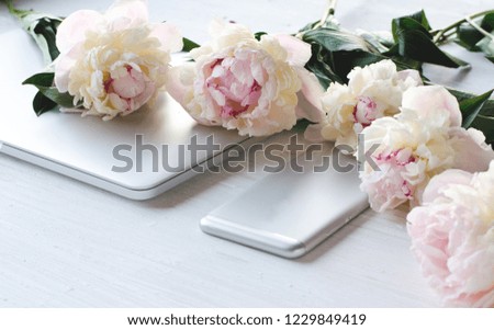 White gentle peonies lie on the smartphone and on the laptop. Place for text. Romantic gift