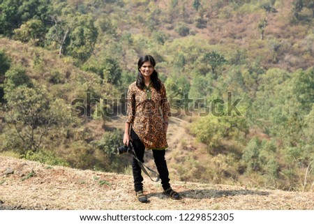 Smiling female photographer using a professional digital camera in natural landscape on background.