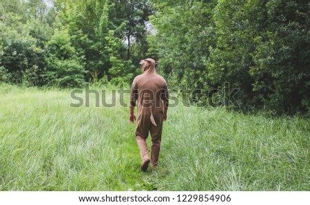 Young man is walking in the forest in cosplay costume of a cow. Guy in the funny animal pajamas sleepwear  in the nature. Halloween ideas for party.
