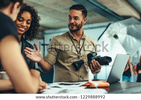 Photographer reviewing the photo shoot with his team on a laptop. Man holding camera discussing photo shoot with his team.