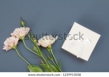 Bouquet of pink flowers with leaves and gift box on gray background. Top view. Celebration day concept.