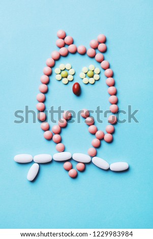 cute owl made of colorful capsules, tablets, pills isolated on blue, sleeping disorders, insomnia treatment, creative concept, flat lay, top view