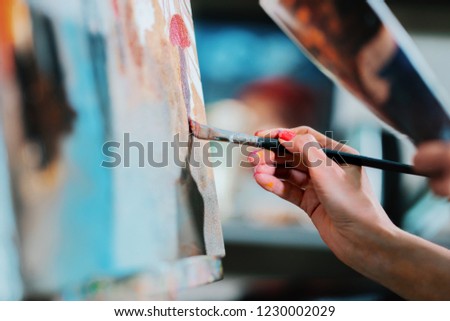 Woman paints a painting on canvas. Art academy or drawing school. Girl paints on the easel. Only hand of unknown artist, brush and canvas.