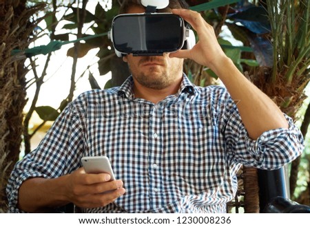 A man in a shirt on his head a virtual reality helmet. Palm tree background