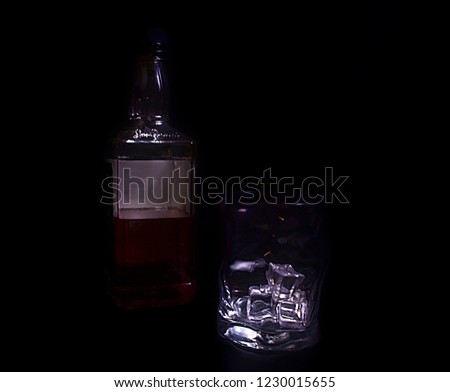 Straight on picture of bottle of whiskey and glass including ice cubes, in black background