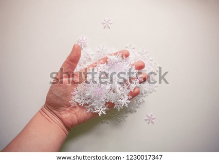 White artificial snowflakes in a woman's hand on soft light background. Winter background. Decorative template for cards, banner, poster.