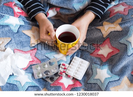 Sick woman under blanket with cup of tea