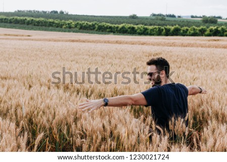 Young man in the wheat field with spread arms  