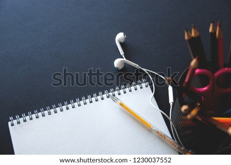 blank landscape sheet, headphones, yellow pen and stand with stationery on dark background with copy space.